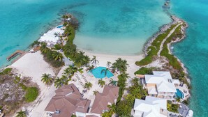 An aerial view of a coastal resort with multiple buildings, a swimming pool, and a beach area.