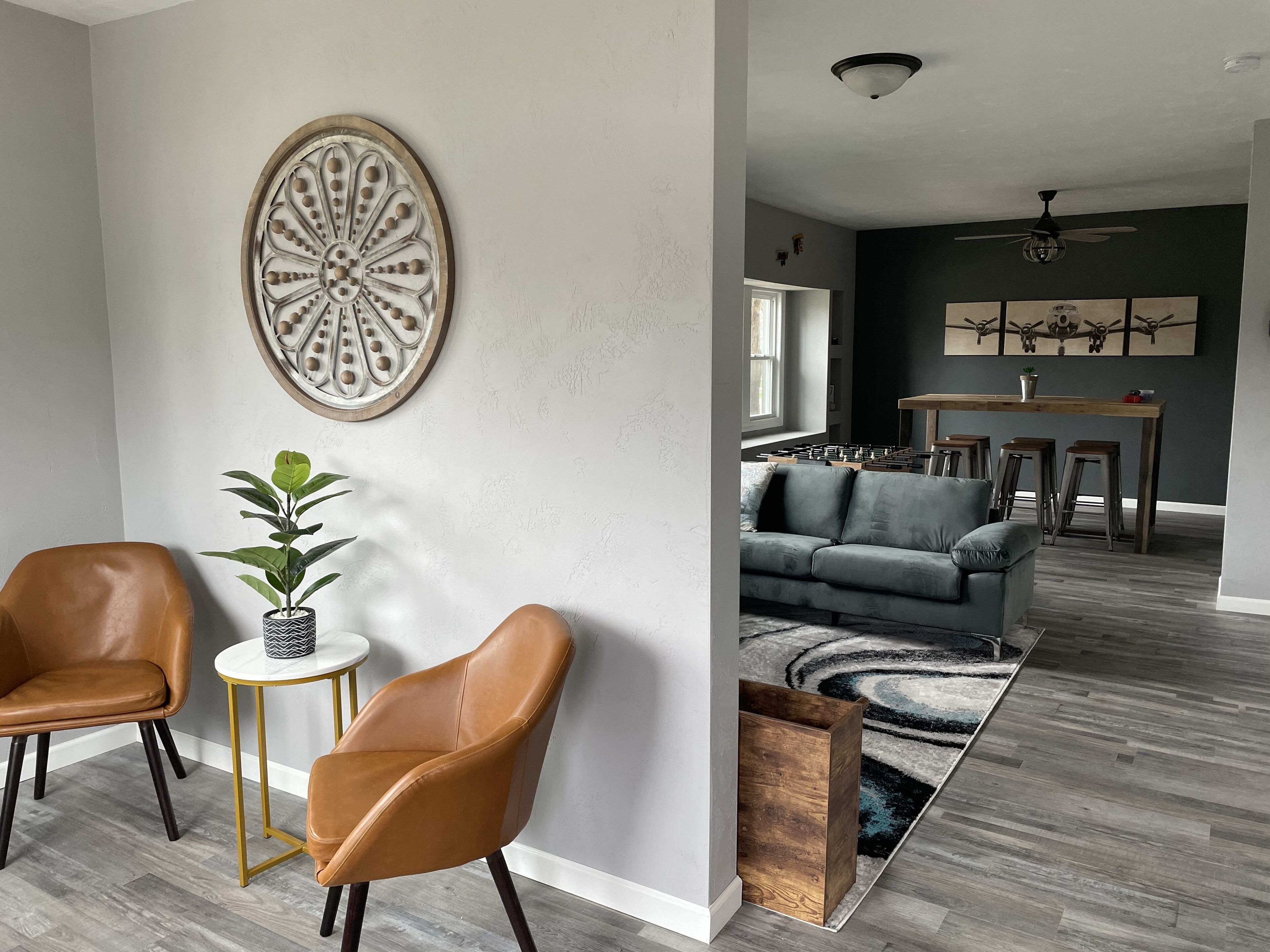 Una sala de estar moderna con un sofá gris, dos sillones de cuero, una mesa de centro y un elemento decorativo en la pared.