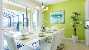 A dining area with a table set for four, white chairs, a chandelier, and a green wall with a painting. - Update Providence golf • Lexurey Villa cul-de-sac • Near Disney
 (Davenport)