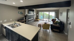 Eine moderne Küche mit einer großen Kochinsel, ein Essbereich mit einer Couch und Stühlen sowie ein Wohnzimmer mit Fernseher.