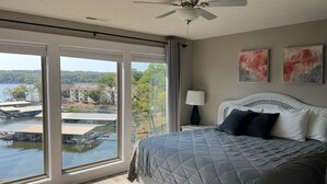 Ein Schlafzimmer mit großem Fenster, einem Bett, einem Deckenventilator und zwei abstrakten Bildern.