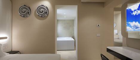 A modern hotel room with a bed, a desk, and a bathroom visible through an open door.