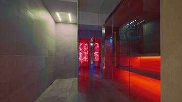 A modern hallway with a glass partition on the right, a red-lit room in the background, and a ceiling light.
