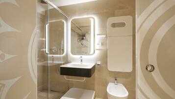 A modern bathroom with a glass-enclosed shower, a pedestal sink, a bidet, and a large mirror.