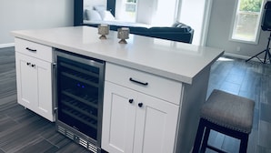 A modern kitchen with a built-in wine cooler, white cabinetry, and a large island with two candle holders.