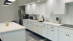 A modern kitchen with white cabinetry, a stainless steel refrigerator, a microwave, and a black faucet.