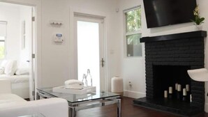 Una sala de estar moderna con una mesa de centro de vidrio, un sofá blanco, una chimenea negra y un televisor montado en la pared.