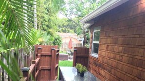 Un patio trasero con una terraza de madera, una mesa con cubierta de vidrio y una pequeña planta en maceta.