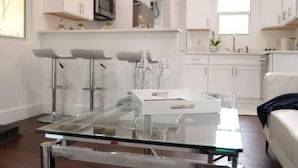 Una cocina moderna con armarios blancos, una mesa de comedor con superficie de vidrio y un horno empotrado.