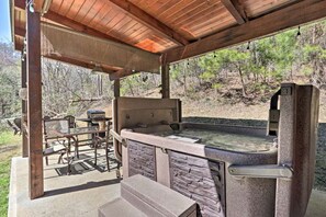 Ein Außenbereich mit Whirlpool, Steinmauern, einer Holzpergola und einem Grill.