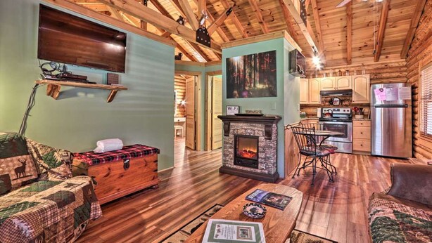 A cozy cabin interior with a fireplace, wooden furniture, a dining area, and a kitchen. - Cozy Log Cabin w/ Hot Tub & Fire Pit! (Sevierville)