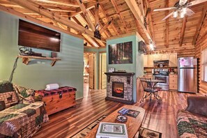 A cozy cabin interior with a fireplace, wooden furniture, a dining area, and a kitchen. - Cozy Log Cabin w/ Hot Tub & Fire Pit! (Sevierville)