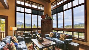 Un amplio salón con ventanas grandes, chimenea, sofás de cuero y una mesa de centro.