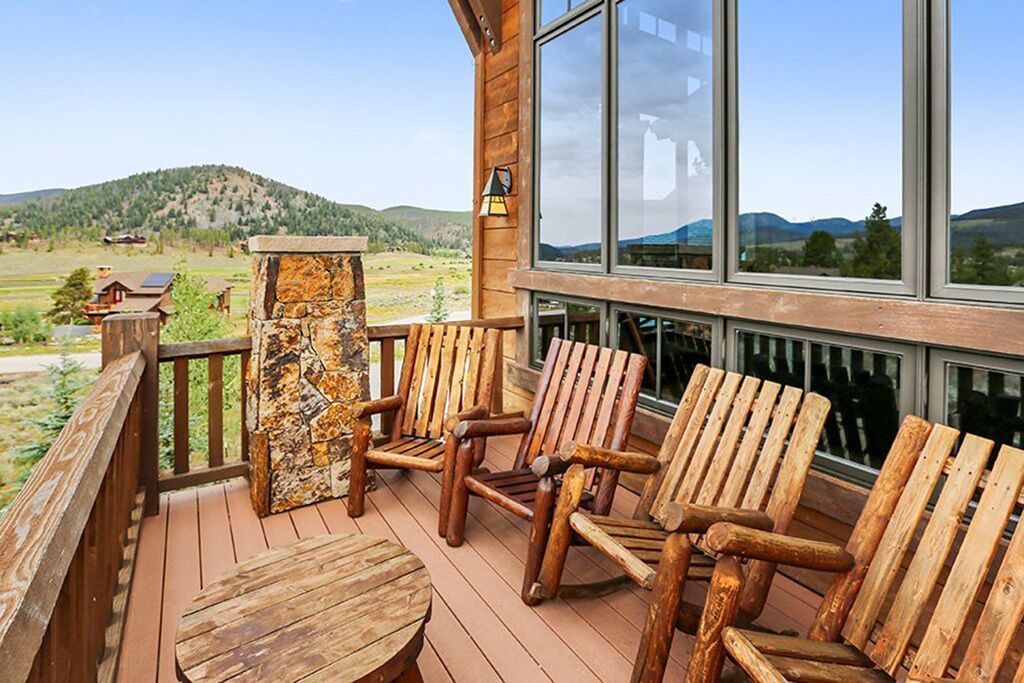 Eine Holzterrasse mit Adirondack-Stühlen und einer Stein Säule, mit Blick auf eine reizvolle Landschaft.