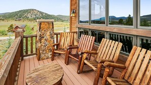 Una terraza de madera con sillas Adirondack y un pilar de piedra, con vistas a un paisaje pintoresco.