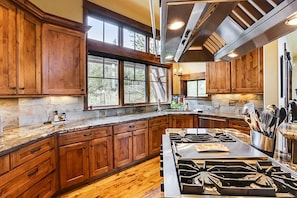 A kitchen with wooden cabinets, a granite countertop, a gas stove, and a window overlooking a wooded area.