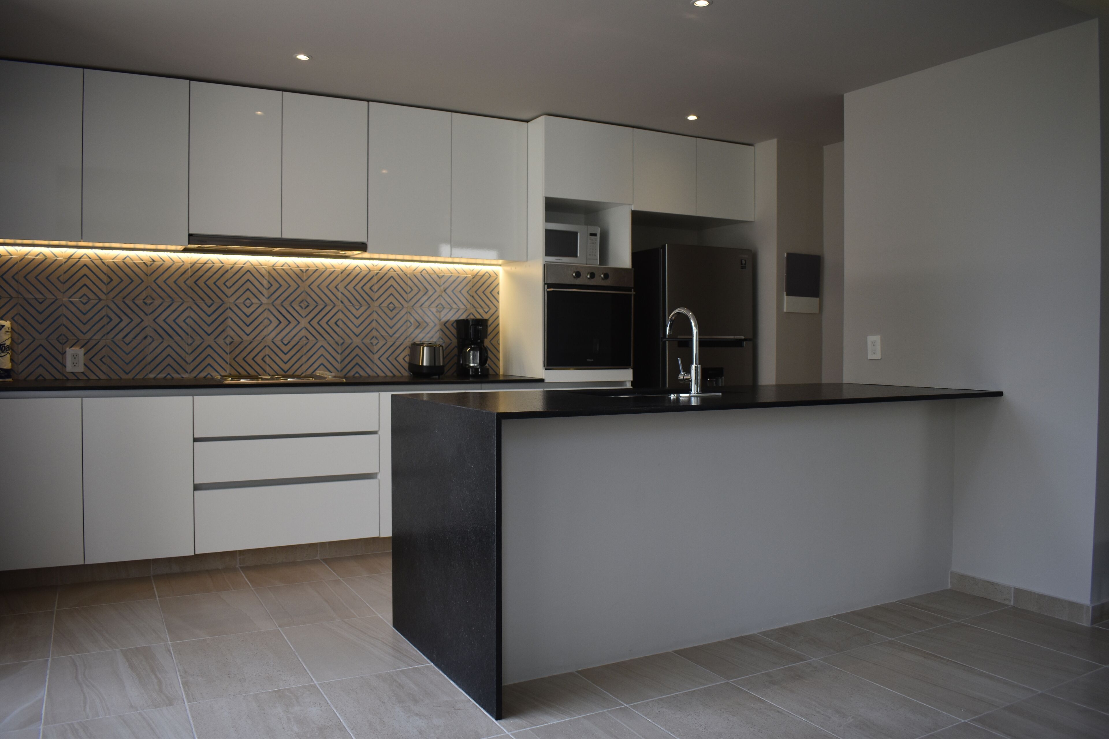 A modern kitchen with white cabinetry, a black countertop island, and a patterned backsplash.