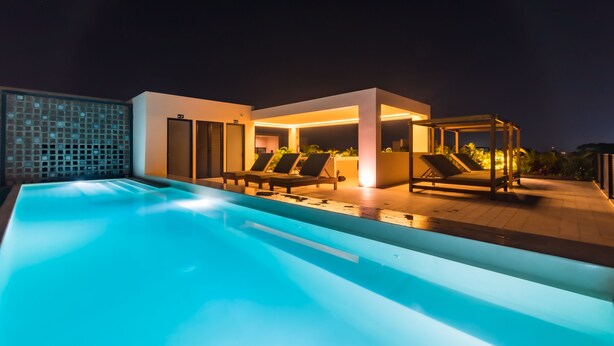 Un área de piscina moderna al aire libre con sillones de descanso y una zona de estar cubierta.