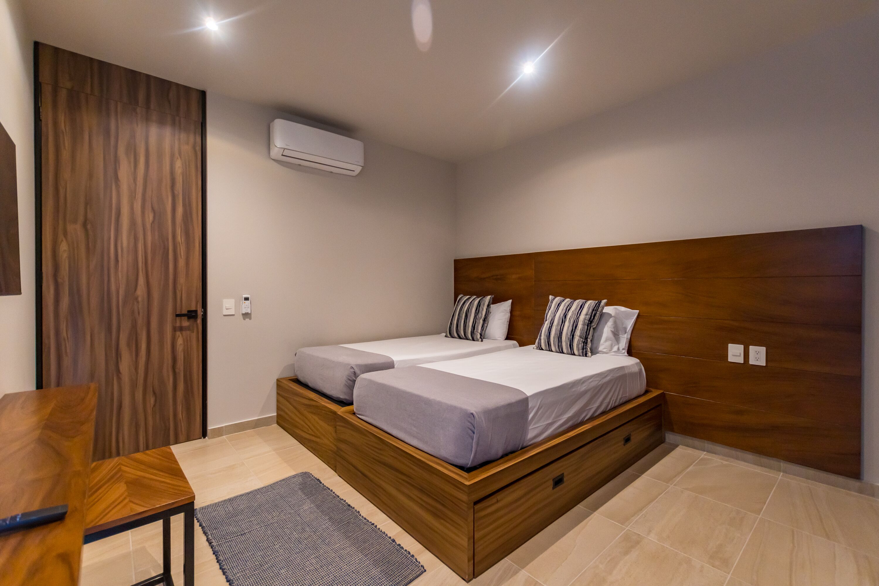 Une chambre à coucher moderne avec un cadre de lit en bois, deux lits, un bureau en bois et un petit tapis.