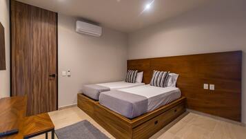 Un dormitorio moderno con estructura de cama de madera, dos camas, un escritorio de madera y una alfombra pequeña.