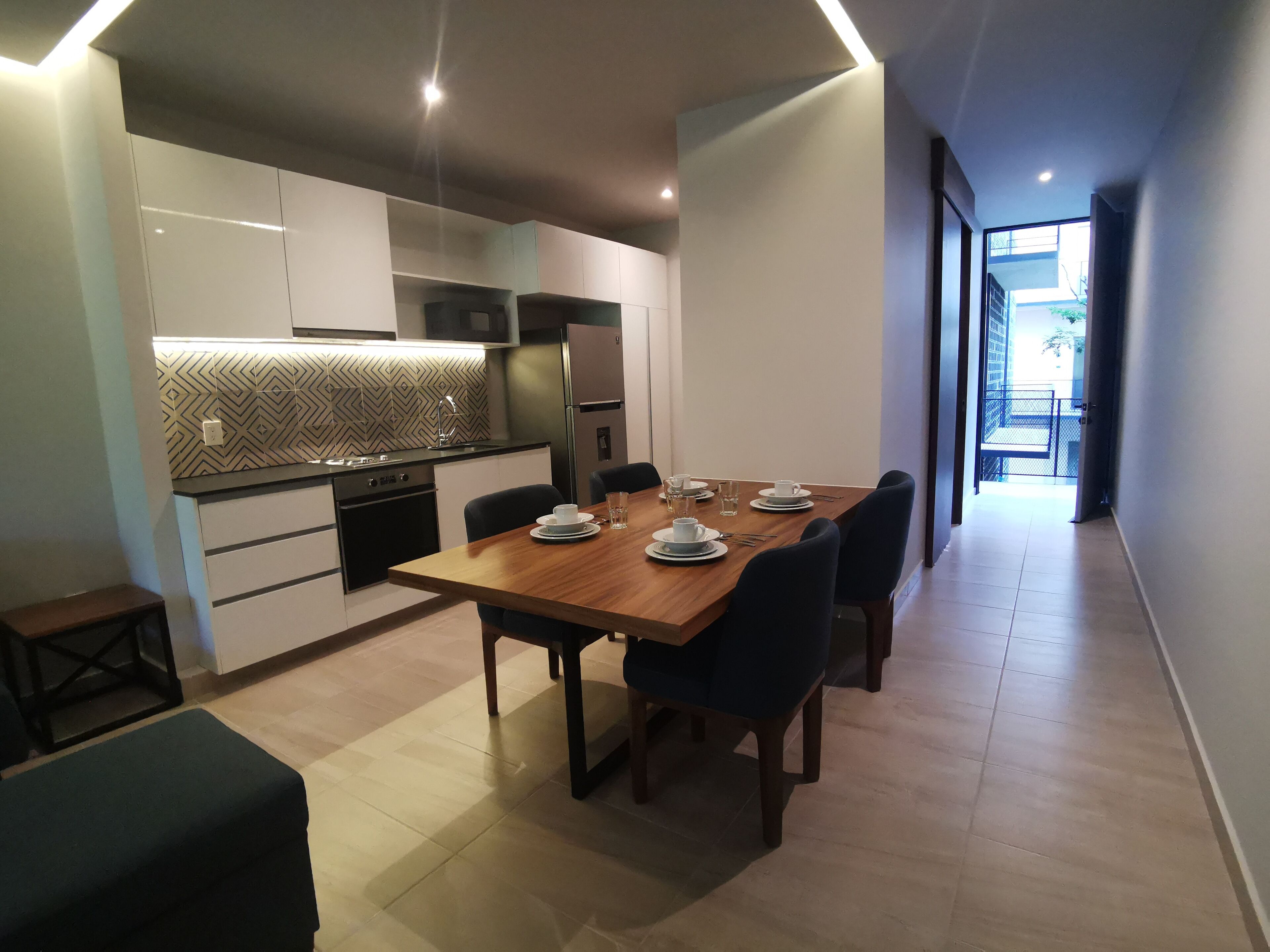 A modern kitchen with white cabinets, a patterned backsplash, and a dining area with a wooden table set for four.