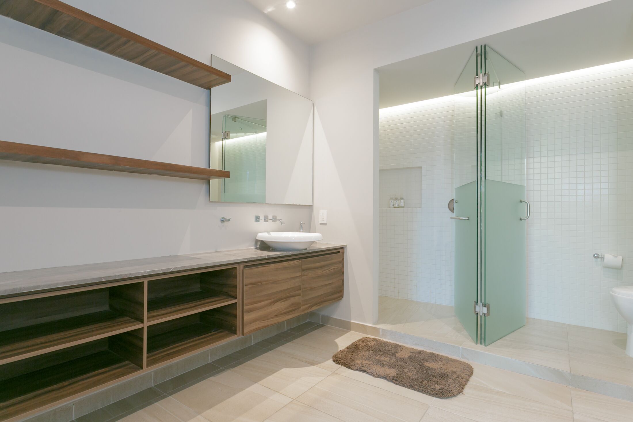 Un baño moderno con ducha envuelta en vidrio, tocador de madera y un espejo grande.