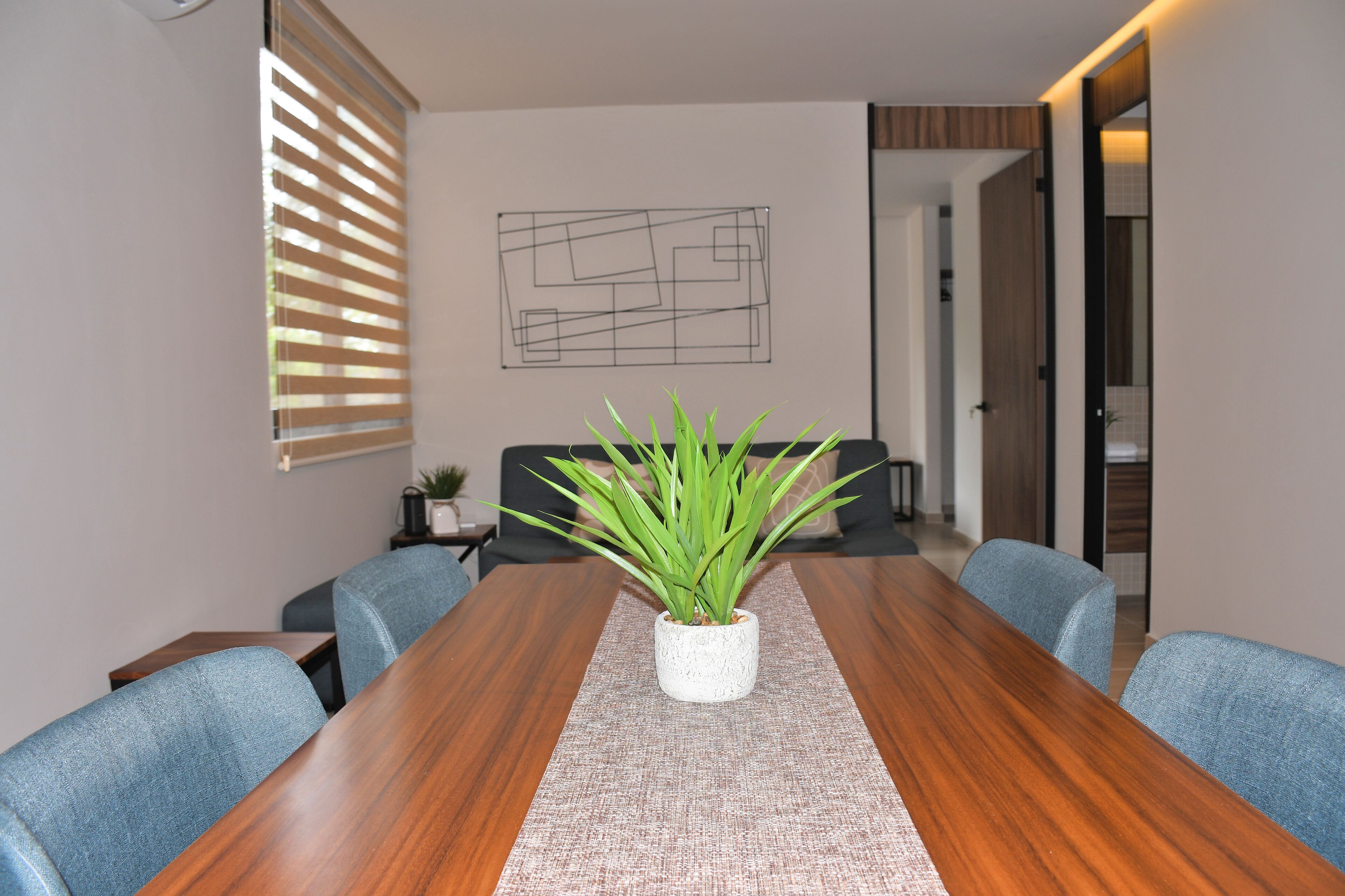 Un salón de conferencias con una mesa de madera, sillas azules y una planta en maceta.