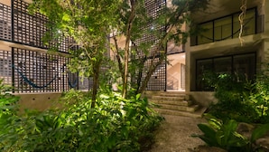 Un camino que lleva a un edificio de diseño moderno, rodeado de abundante vegetación y una valla decorativa.