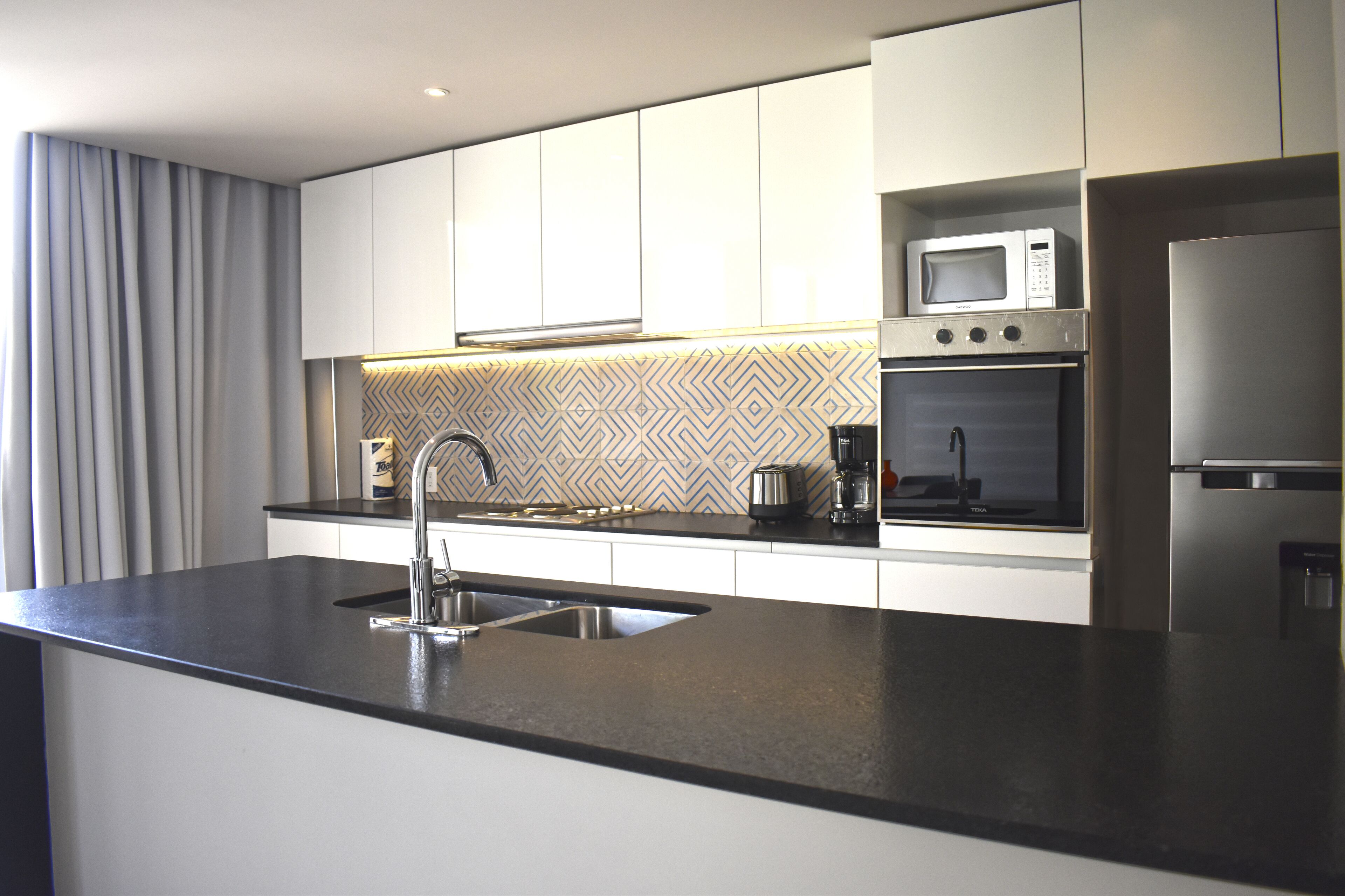 A modern kitchen with a black countertop, stainless steel appliances, and a patterned backsplash.