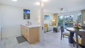 Una cocina moderna con una isla central, un comedor con una mesa redonda y sillas, y una sala de estar con sofá y vistas al exterior.