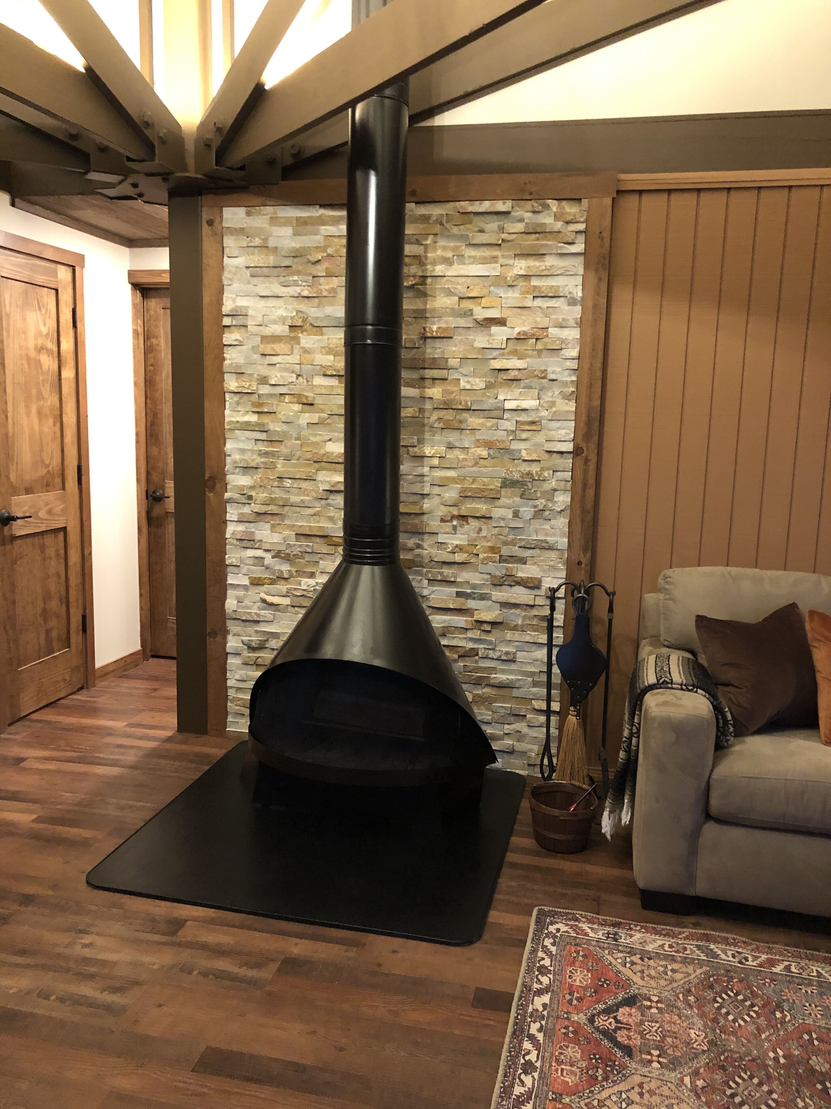A cozy living room with a stone wall, a fireplace, a wooden floor, and a sofa.