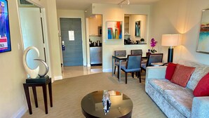 A living room with a sofa, coffee table, and chairs. There is a kitchen area in the background with a dining table and chairs. - 5 Stars Apart-Suites by Hilton. Amazing views. (Fort Lauderdale)