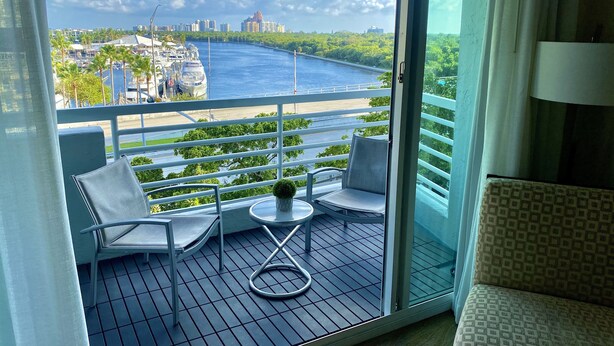A balcony with two chairs, a small table, and a view of a river and cityscape. - 5 Stars Apart-Suites by Hilton. Amazing views. (Fort Lauderdale)