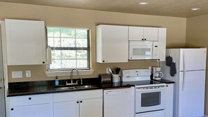 Une cuisine de taille réduite, avec des meubles blancs, un four à micro-ondes, un réfrigérateur, un évier et une cuisinière.