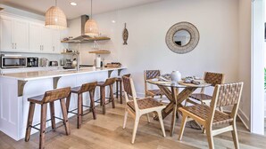 Een moderne keuken met witte kastjes, houten krukken en een ronde eettafel.