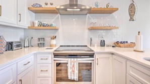 Een moderne keuken met witte kasten, roestvrijstalen apparatuur en houten planken.