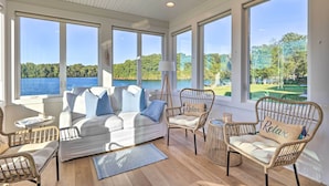 Ruime kamer met een witte bank, rieten stoelen en uitzicht op een meer en golfbaan.