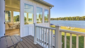Een houten terras met een tafel en stoelen, een overdekte patio met uitzicht op het meer, en een gazon met buitenmeubels.