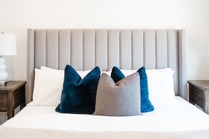 Comfortable bed with a light-colored headboard, accompanied by a bedside table and lamp.