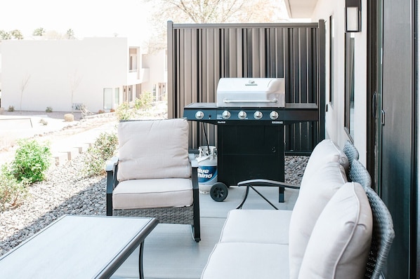 Enjoy al fresco dining and relaxation on this outdoor patio with a grill station, wicker chair, and comfortable sofa.