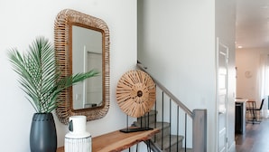 Een modern interieur met een houten console, een grote spiegel, een decoratief wandobject en een potplant.