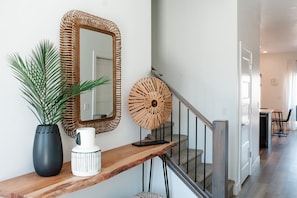 Relax in a serene space with a console table, woven mirror, and lush greenery.
