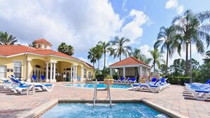 A swimming pool with lounge chairs and a covered area, surrounded by palm trees and a building with a red roof. - Be-Our-Guest Home! 7 bdrm incl. 5 King beds, Private POOL, 15 minutes to Disney! (Kissimmee)