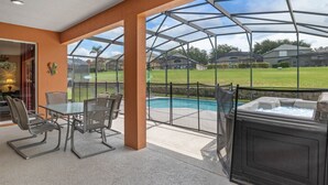 A covered patio area with a glass enclosure, a hot tub, and a pool. - Be-Our-Guest Home! 7 bdrm incl. 5 King beds, Private POOL, 15 minutes to Disney! (Kissimmee)