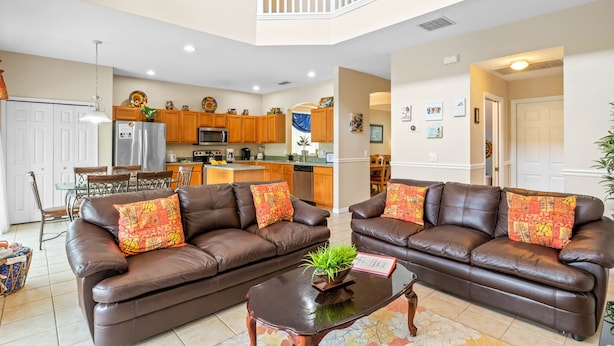 A spacious living room with two brown leather sofas, a coffee table, and a dining area with wooden chairs and a glass table. - Be-Our-Guest Home! 7 bdrm incl. 5 King beds, Private POOL, 15 minutes to Disney! (Kissimmee)