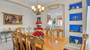 A dining area with a wooden table, chairs, a chandelier, and a wall with decorative items and a sign. - Be-Our-Guest Home! 7 bdrm incl. 5 King beds, Private POOL, 15 minutes to Disney! (Kissimmee)