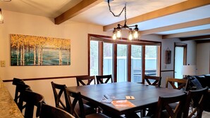 Un'area pranzo con un grande tavolo di legno e sedie, un quadro appeso al muro e vista attraverso le porte in vetro.