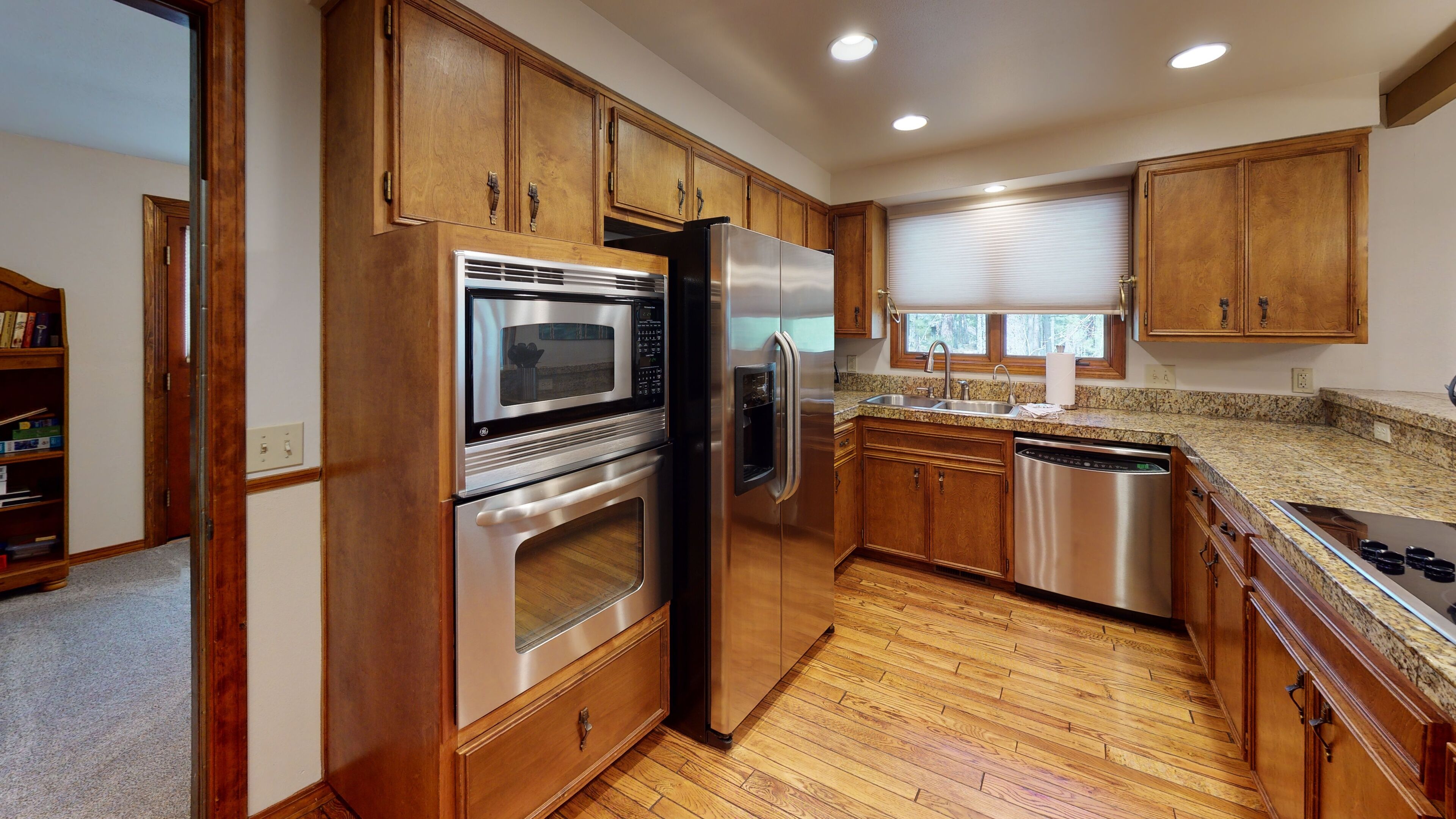 A kitchen with wooden cabinets, stainless steel appliances, granite countertops, and a window with blinds.