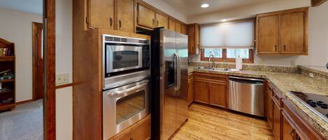 A kitchen with wooden cabinets, stainless steel appliances, granite countertops, and a window with blinds.