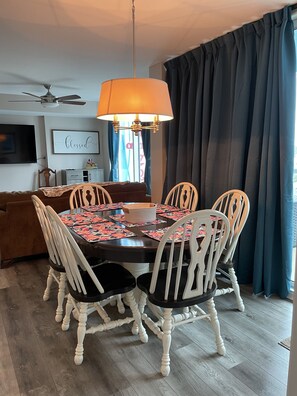 Uma sala de jantar com uma mesa redonda, cadeiras brancas, um lustre e um ventilador de teto.
